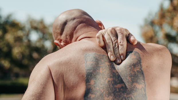 Bald man with tattoo holding back in pain under sunny conditions.